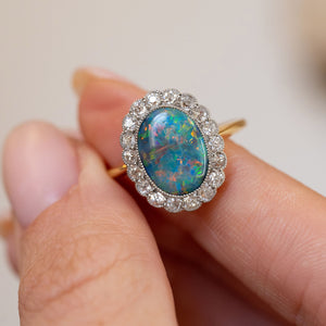Handheld close-up of the black opal’s blue, green and fiery orange tones framed by a halo of diamonds.