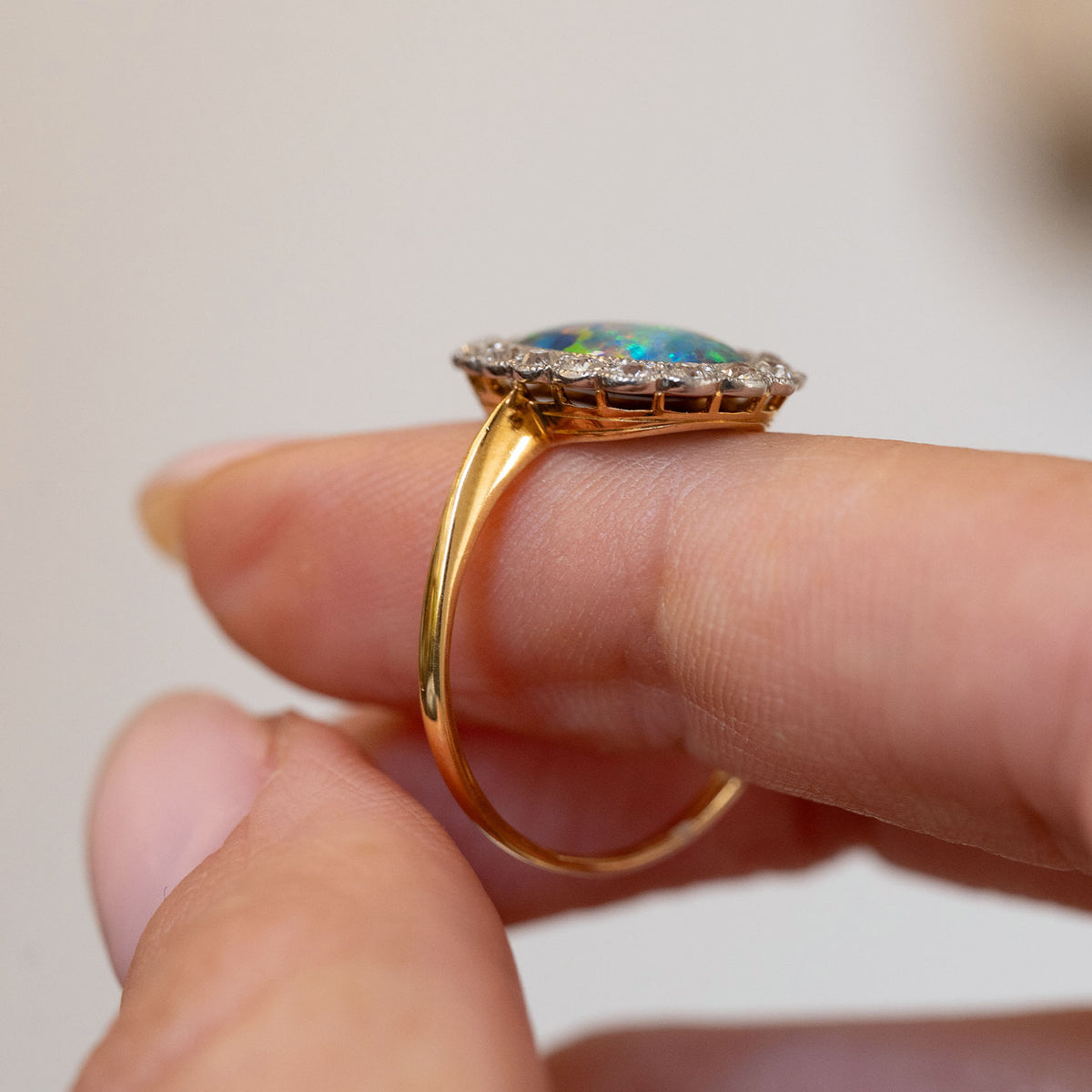 Profile view of the antique cluster ring, displaying the low-set oval opal, platinum gallery and polished yellow gold shank.