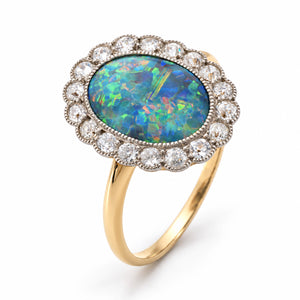 Elevated studio portrait of the Edwardian opal ring, revealing its oval gemstone, scalloped diamond halo and yellow gold shank.