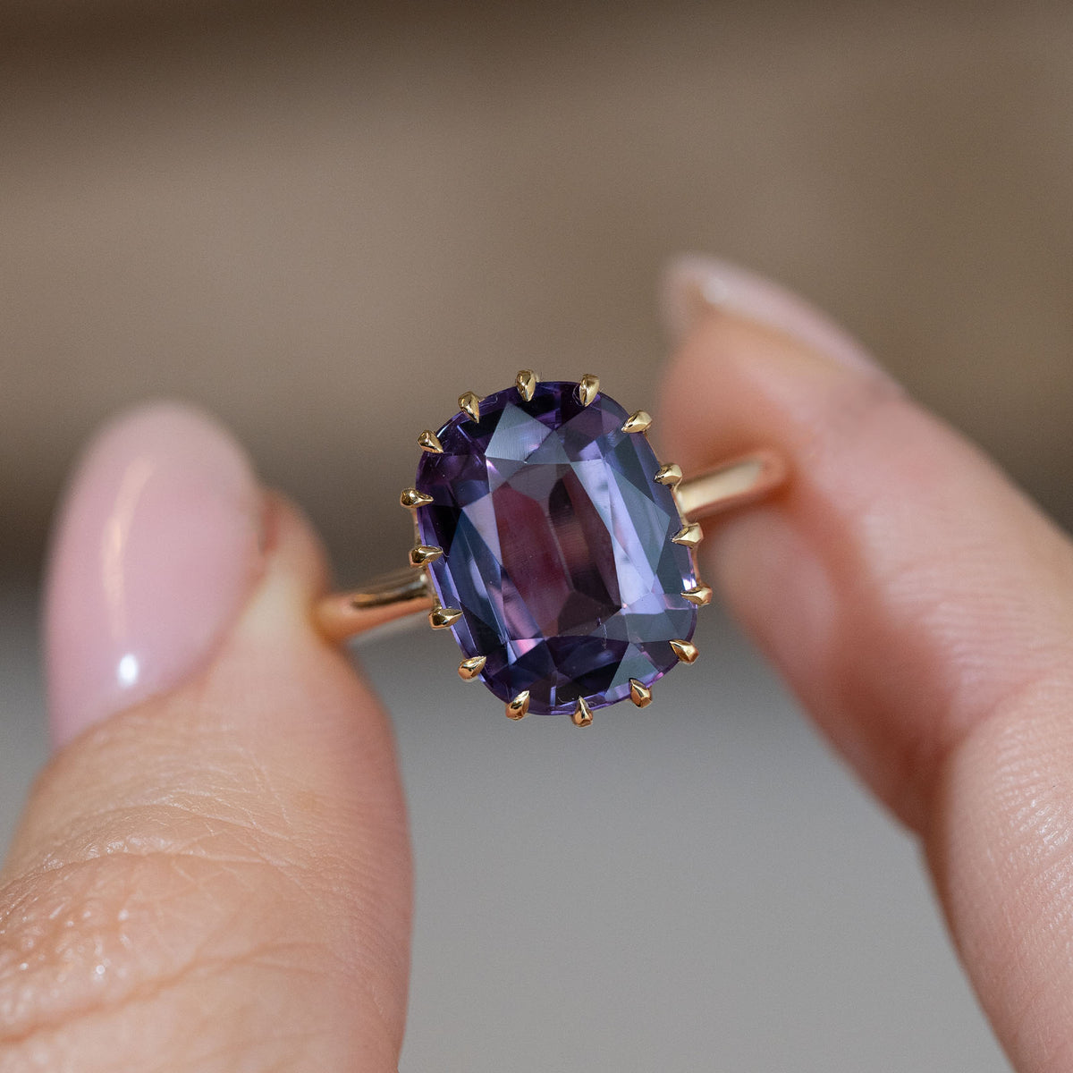 Hand-held close-up of the large violet-blue sapphire, showcasing its rectangular cushion cut and distinctive gold claws.