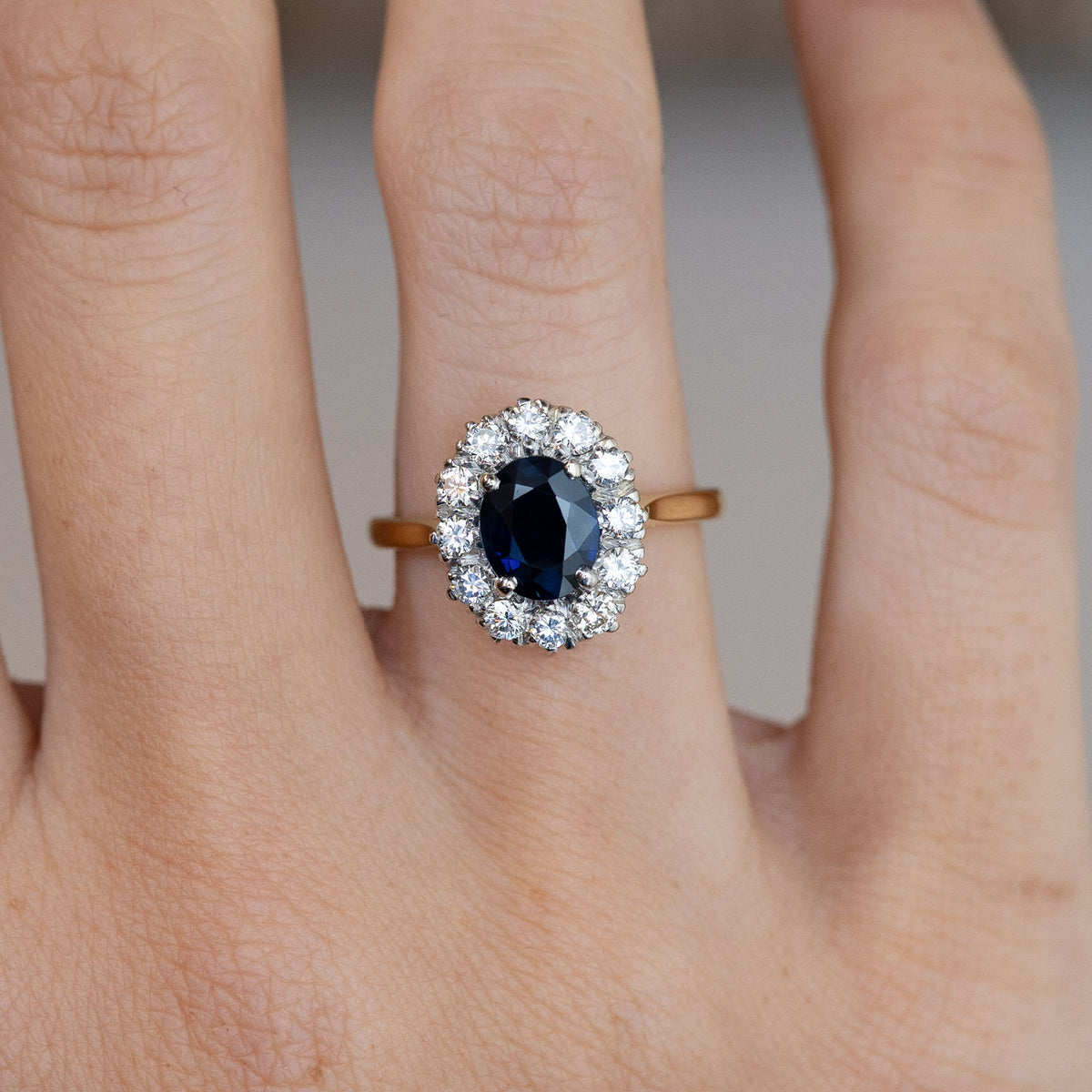 Close-up of the oval dark blue sapphire framed by brilliant-cut white diamonds, worn on a finger.
