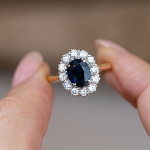 Hand-held close-up of the deep blue oval sapphire surrounded by sparkling white diamonds in a classic cluster setting.