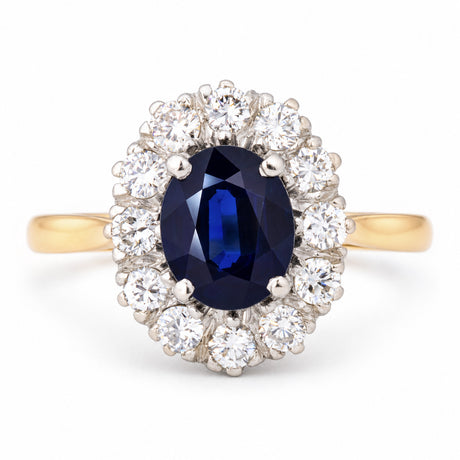 Vintage 1940s dark blue oval sapphire and diamond cluster engagement ring in platinum and yellow gold, surrounded by brilliant-cut white diamonds.