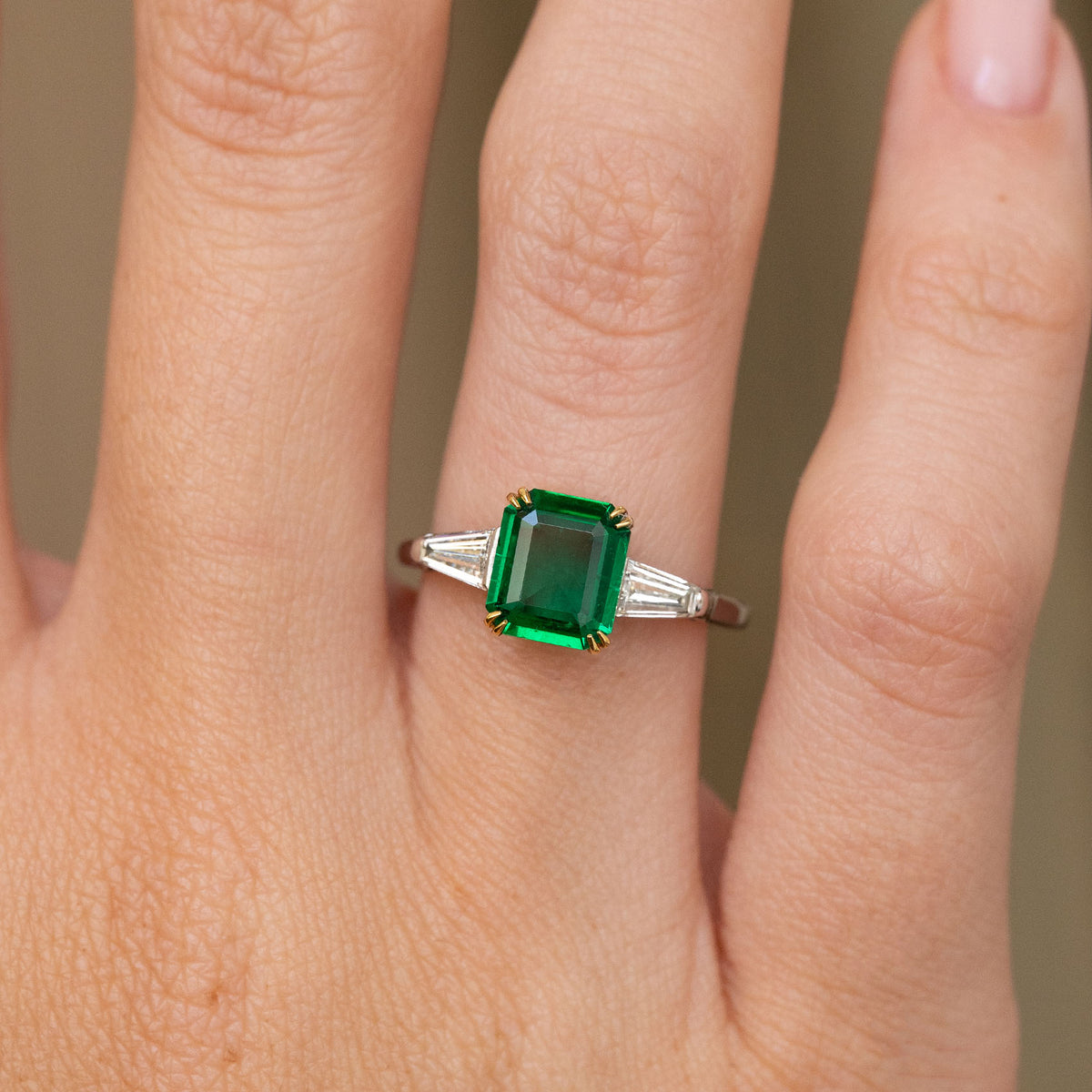 Close hand detail highlighting the rectangular emerald, geometric side diamonds and polished white gold band.