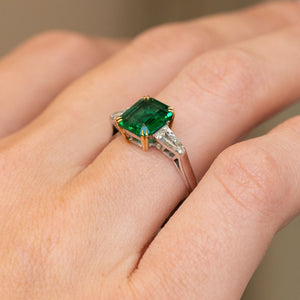 Side-angled view of the vintage engagement ring being worn, displaying the elevated emerald setting and tapered trapezoid diamonds.