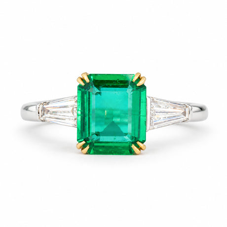 Vintage emerald and diamond three-stone engagement ring, featuring an emerald-cut centre stone flanked by two trapezoid diamonds on a white gold band.