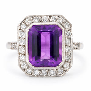 Antique Art Deco amethyst and diamond cluster ring in white gold, featuring a rectangular emerald-cut purple amethyst surrounded by a geometric halo of round diamonds with milgrain detailing.