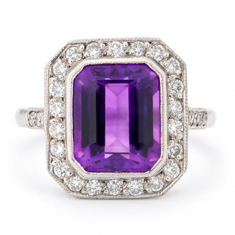 Antique Art Deco amethyst and diamond cluster ring in white gold, featuring a rectangular emerald-cut purple amethyst surrounded by a geometric halo of round diamonds with milgrain detailing.