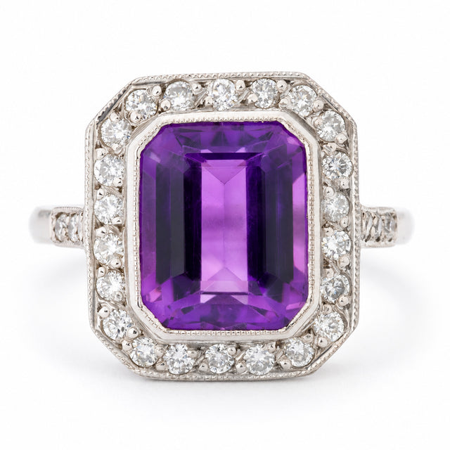 Antique Art Deco amethyst and diamond cluster ring in white gold, featuring a rectangular emerald-cut purple amethyst surrounded by a geometric halo of round diamonds with milgrain detailing.