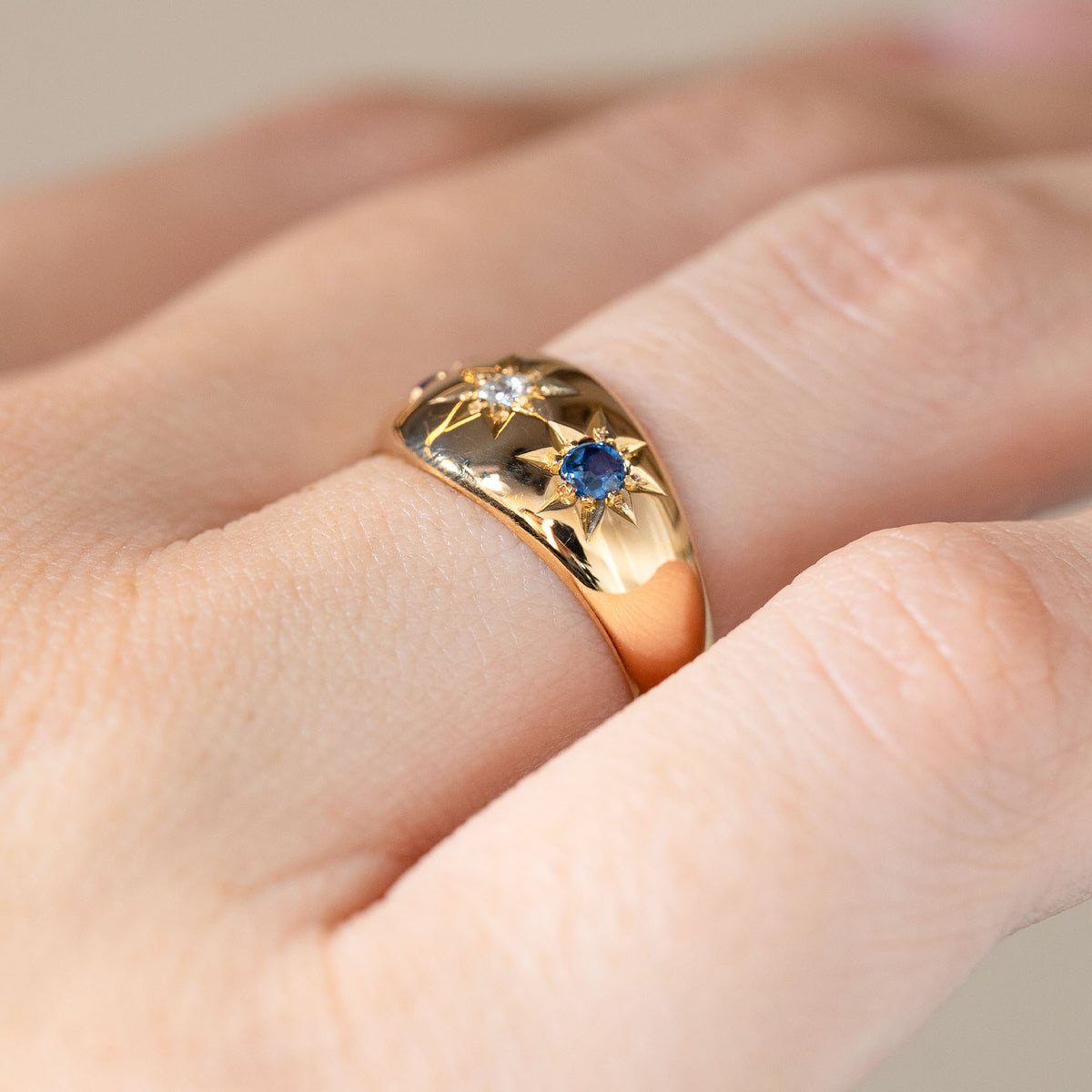 The Edwardian yellow gold ring photographed at an angle on a hand, showing its curved band and flush-set sapphire and diamond arrangement.