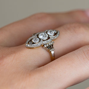 Side angle of the vintage diamond ring worn on a finger, revealing its raised setting, decorative gallery and contrasting yellow gold band.