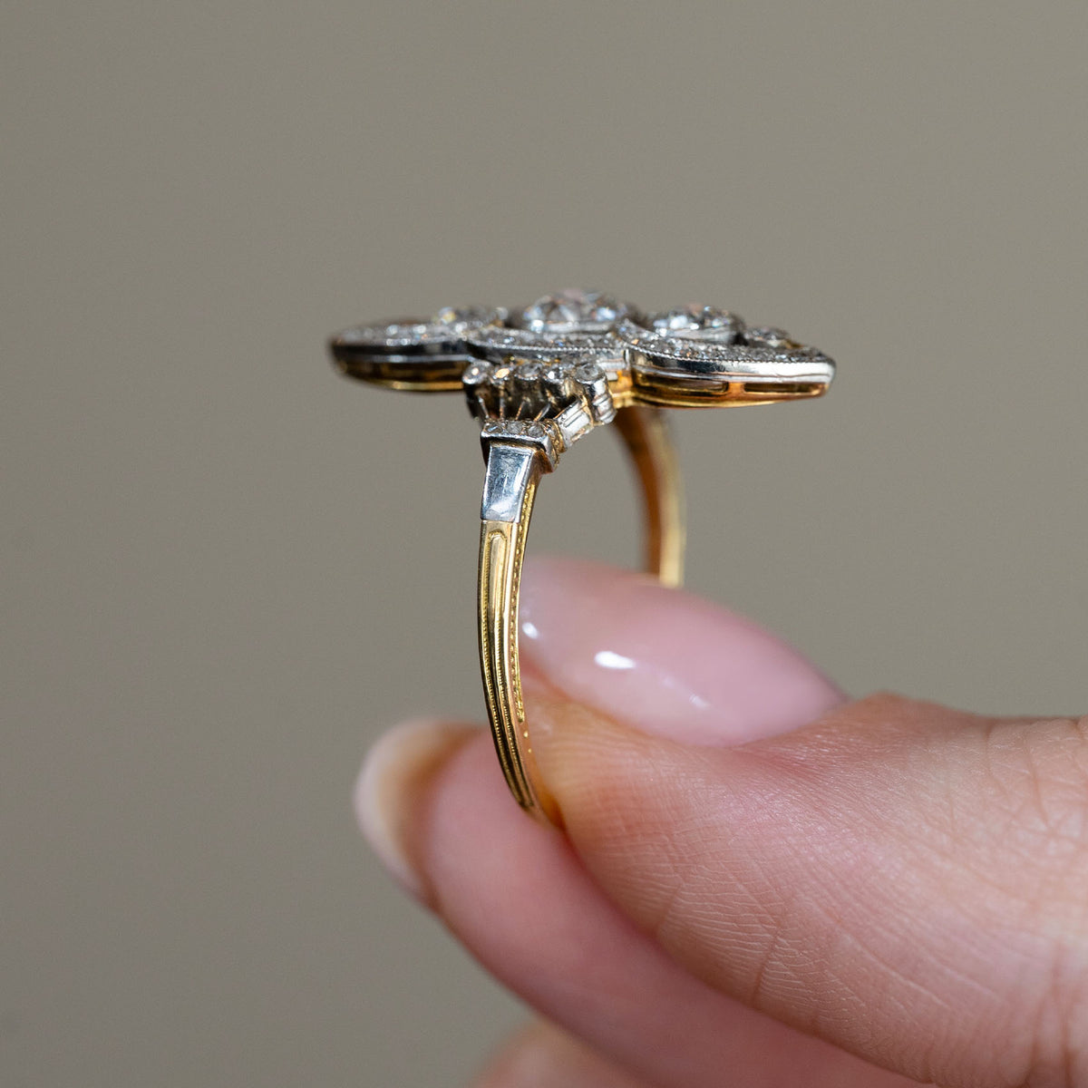 Side profile of the antique platinum and yellow gold ring held between fingers, showcasing the elevated diamond setting, intricate metalwork and slender band.