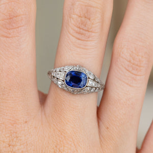 Close hand shot of a Belle Époque platinum ring with a deep blue sapphire framed by rose-cut diamonds and fine milgrain borders.