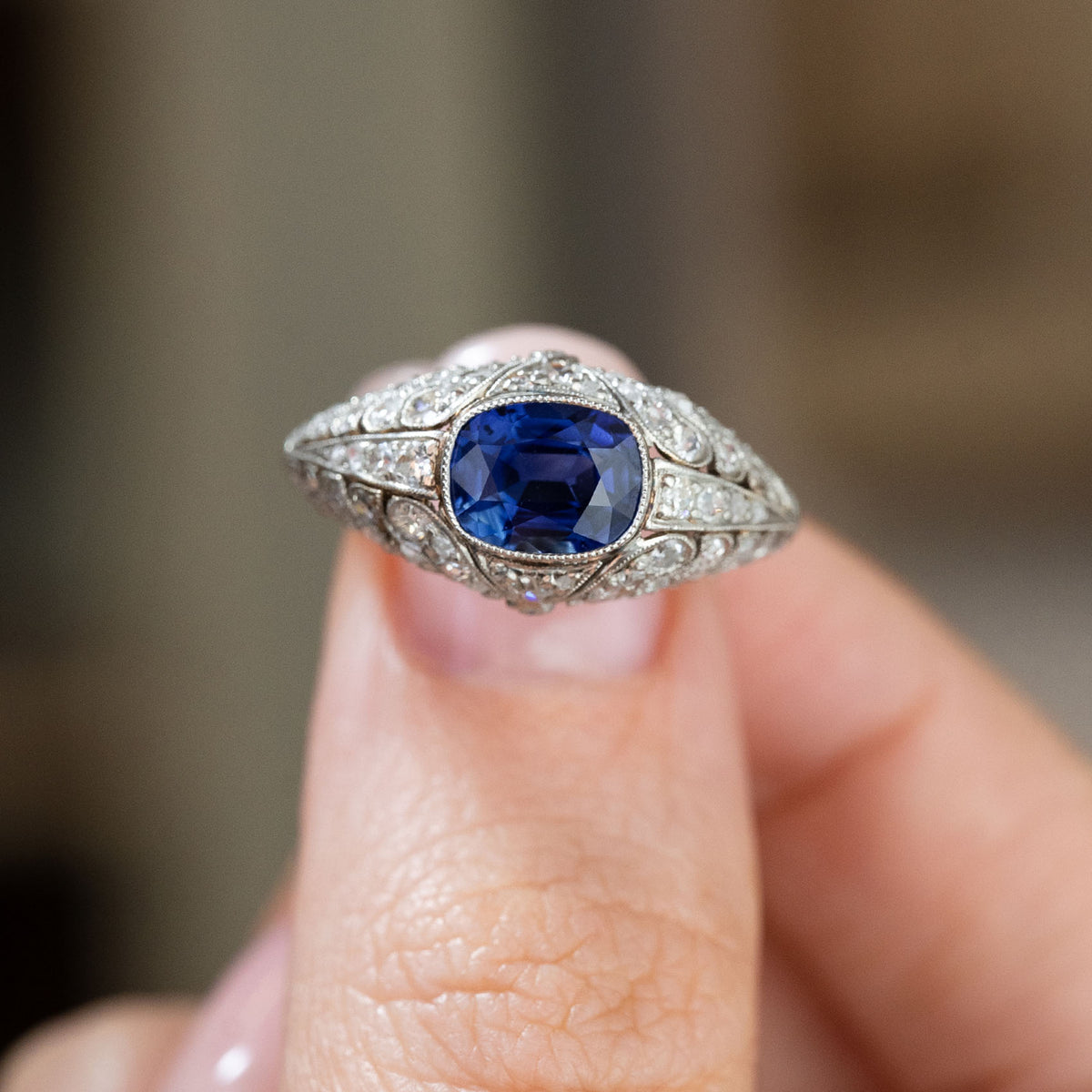 Fingertip close-up of an antique Belle Époque cocktail ring, emphasising the blue sapphire and symmetrical rose-cut diamond design.