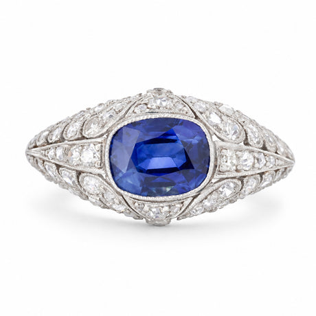 Antique Belle Époque platinum bombé ring centred with a vivid blue sapphire amid sweeping panels of rose-cut diamonds.