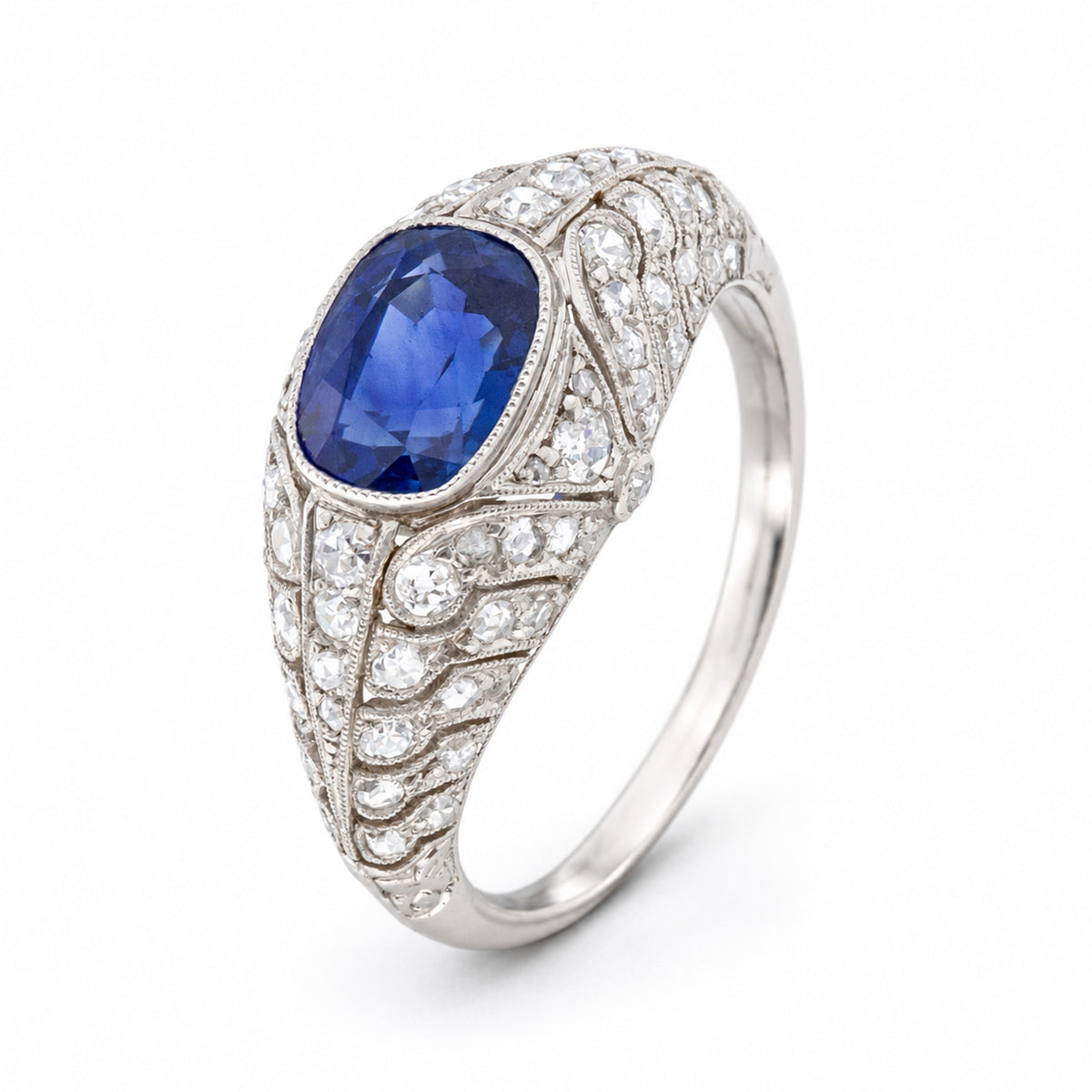 Three-quarter perspective of an antique blue sapphire ring, revealing the sculptural diamond-set bombé form and engraved platinum details.