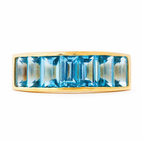 A yellow gold vintage half eternity Swiss blue topaz ring from the 1980s against a plain white background.