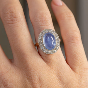 Close hand detail highlighting the pale blue cabochon sapphire, antique-cut diamond cluster and silver-topped setting.