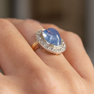 Low angled view of the antique ring being worn, emphasising the sapphire’s high domed profile and sparkling diamond border.