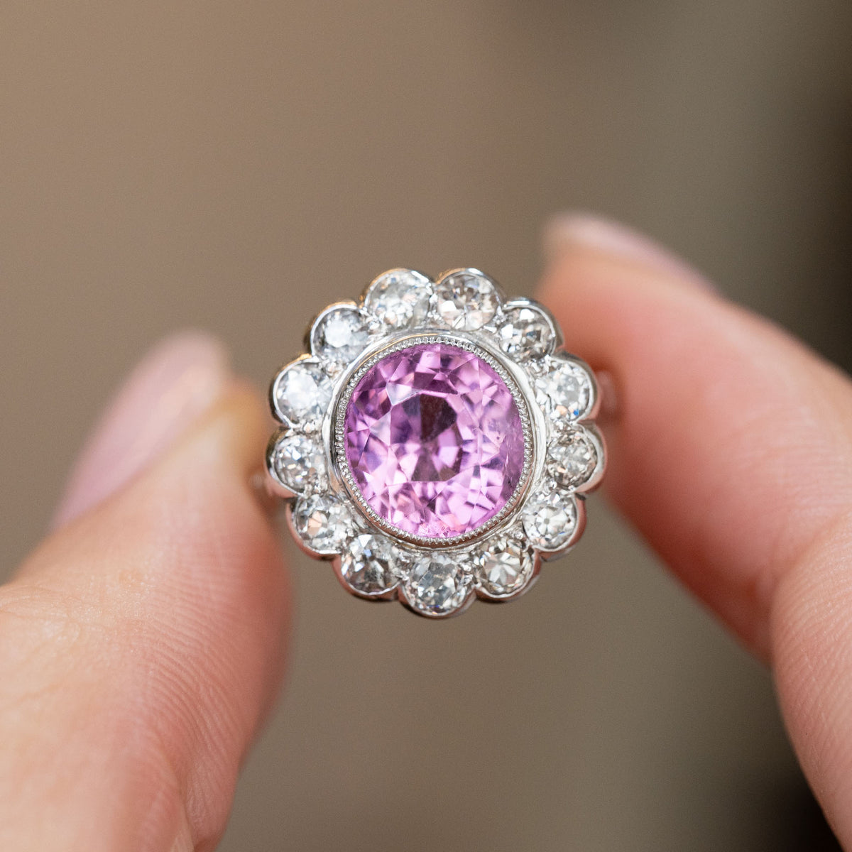 Vintage pink sapphire and diamond ring held between the fingers, offering a detailed look at its flower-shaped cluster.