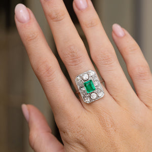 Art Deco emerald and diamond cluster ring worn on the hand, displaying its bold geometric proportions and fine platinum craftsmanship.