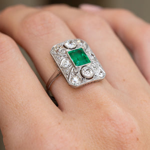 Close-up on-hand view of the platinum panel ring, with a rectangular emerald framed by old-cut diamonds and delicate filigree.