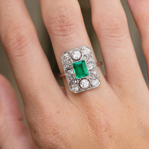 Detailed hand view of the antique emerald ring, showing two prominent rub-over set old-cut diamonds within the openwork panel.