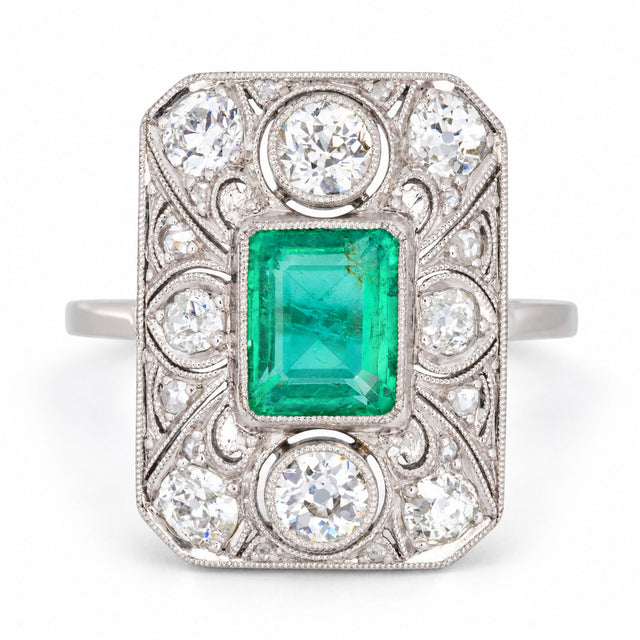Antique Art Deco Colombian emerald and diamond panel cluster ring in platinum, featuring a rub-over set emerald, old-cut diamonds and intricate filigree lacework.