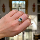 antique oval cut aquamarine singe stone ring worn on closed hand.