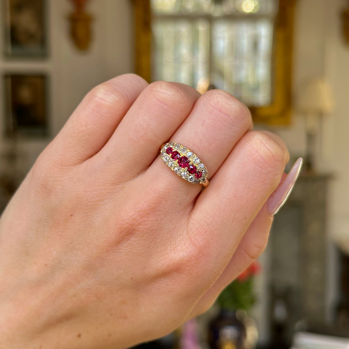 Ruby and diamond cluster engagement ring worn on closed hand. 