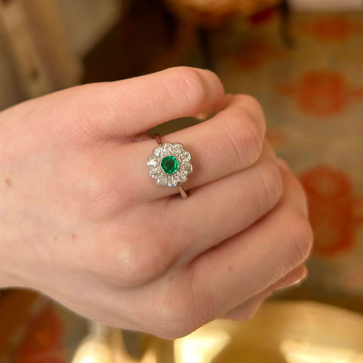 Antique emerald and diamond cluster flower ring in platinum worn on the hand up close to show details