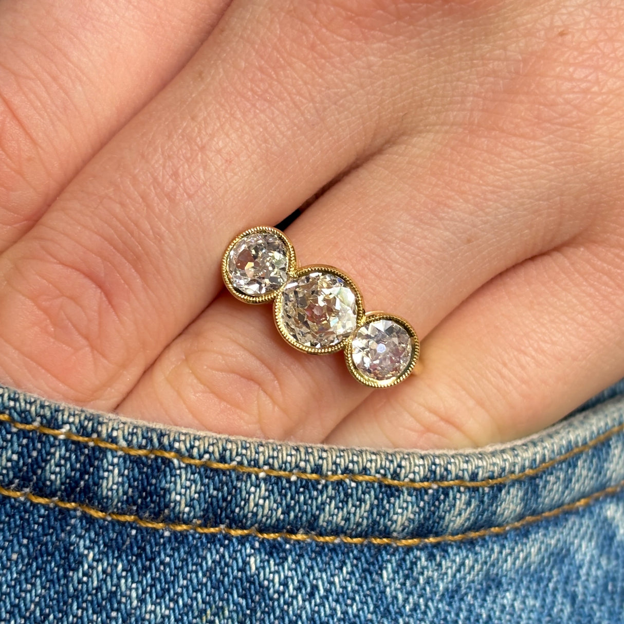Antique, Victorian three-stone diamond ring worn on hand in pocket of jeans