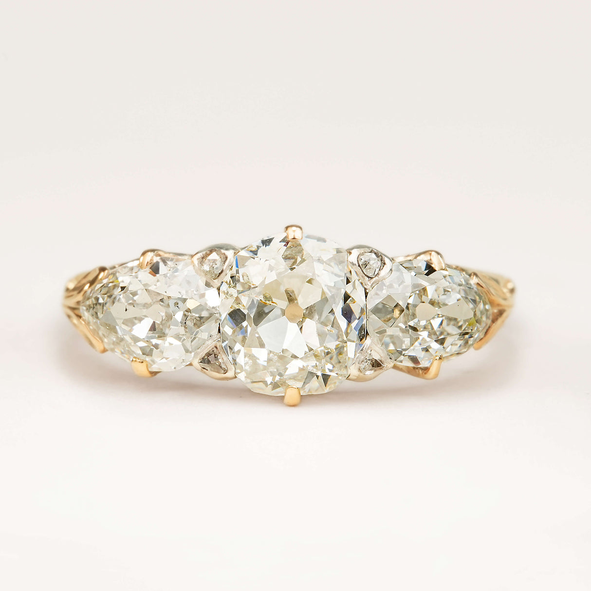 An antique Victorian three-stone engagement ring featuring cushion-cut and pear-cut diamonds, displayed on a clean white background.