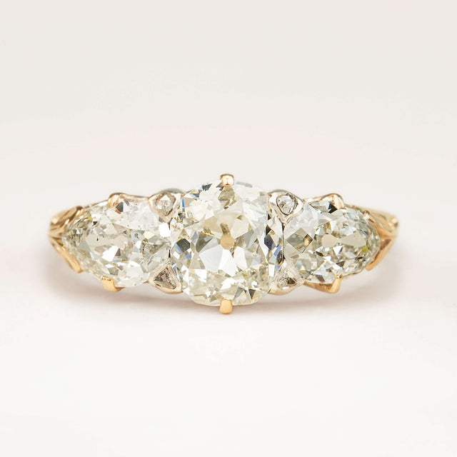 An antique Victorian three-stone engagement ring featuring cushion-cut and pear-cut diamonds, displayed on a clean white background.