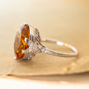 An antique ring with a orange citrine gemstone set in platinum with diamonds in the shoulders. 