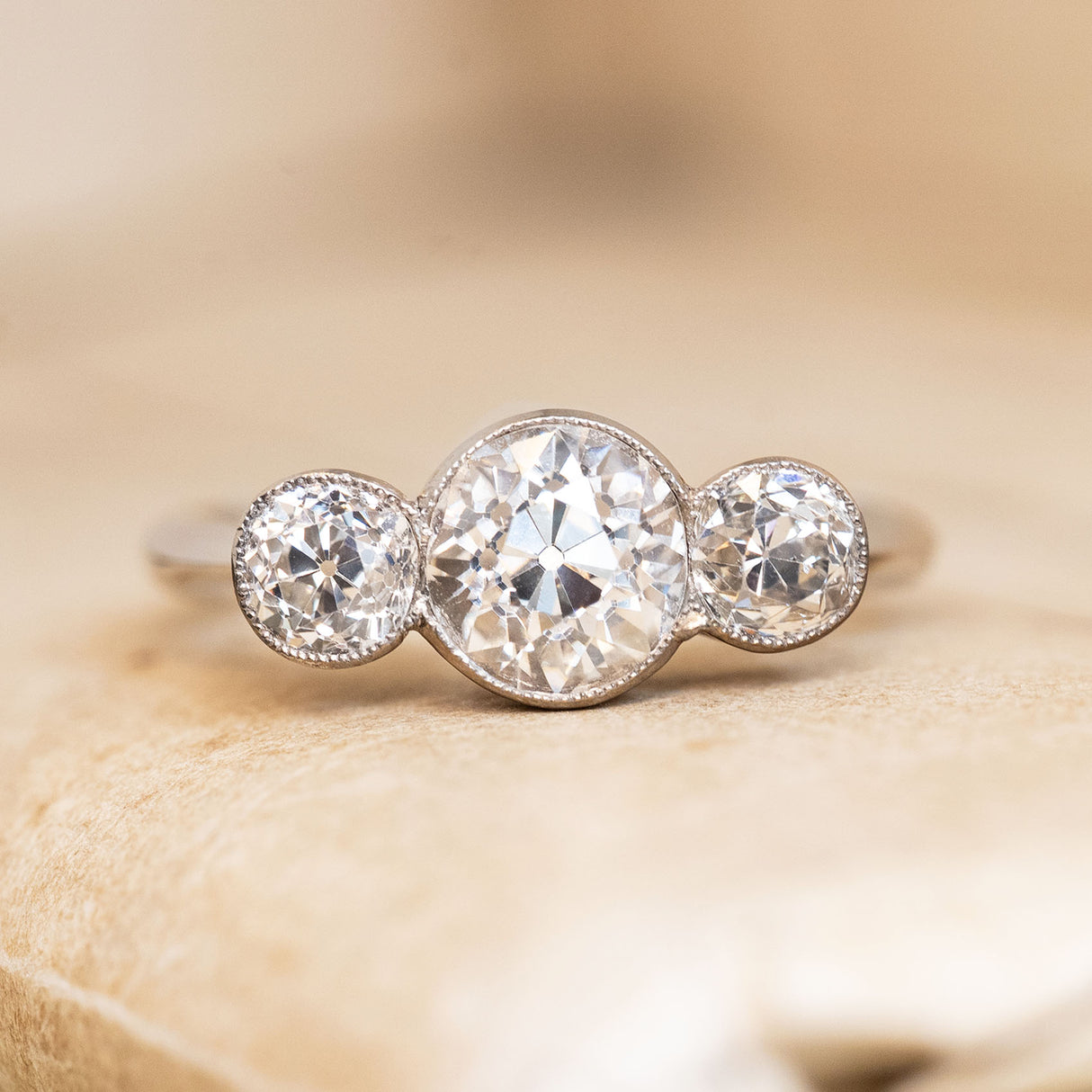 Antique, Art Deco old-cut diamond three-stone ring on a beige book background.