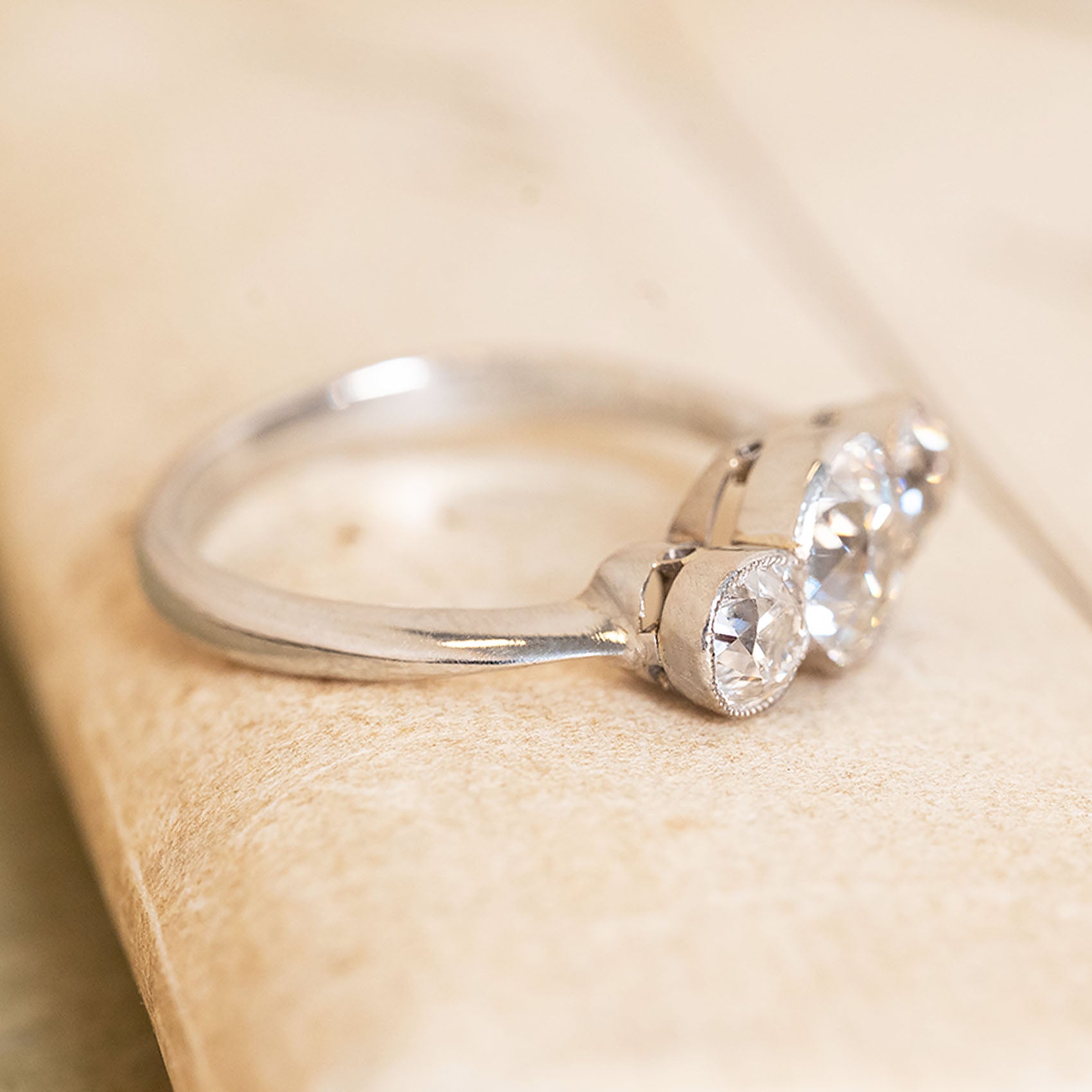 Antique Art Deco old-cut diamond three-stone ring with a larger central diamond, in a rub-over platinum setting.