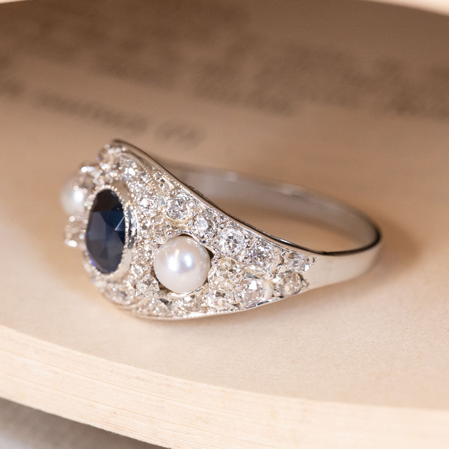 A gold antique dark blue sapphire pearl gold ring with a diamond cluster displayed on book pages.