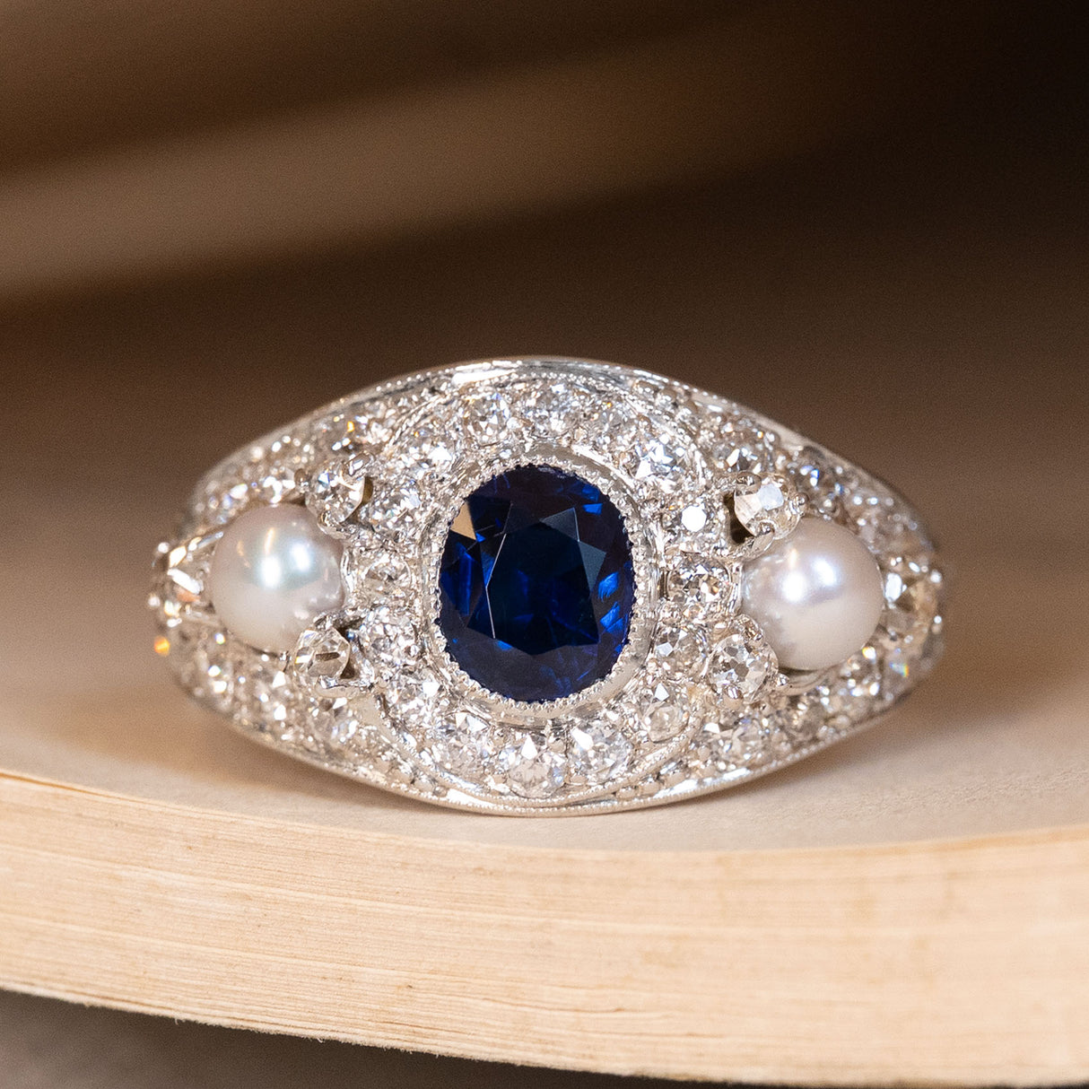 Antique Belle Epoque blue sapphire pearl and diamond cluster gold ring displayed on a book.