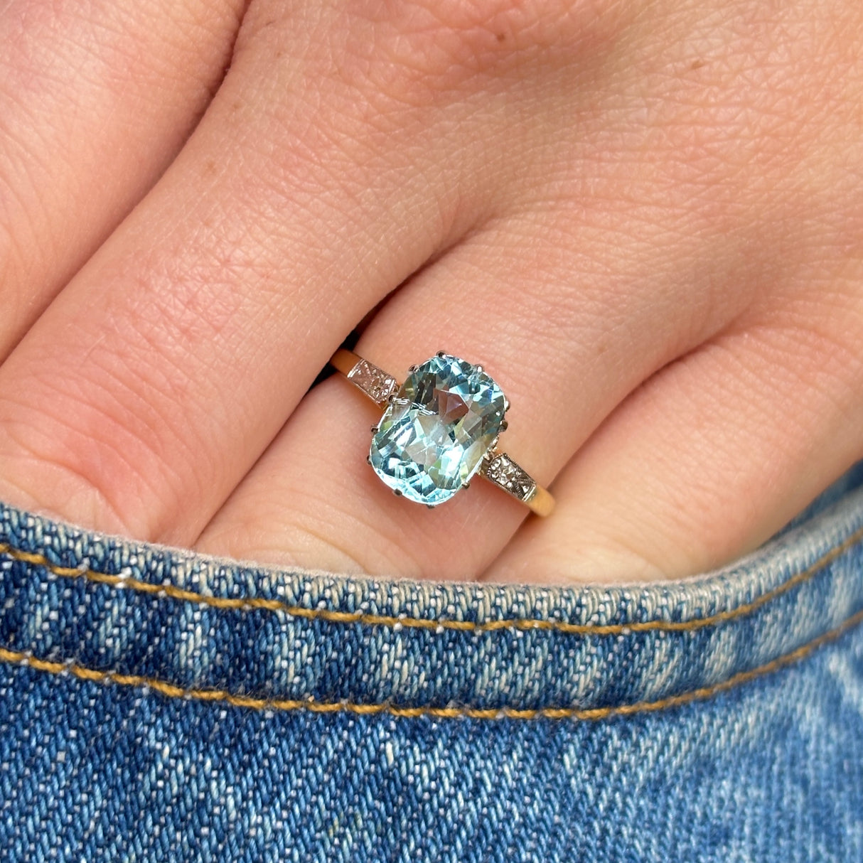 Antique Edwardian cushion-cut aquamarine and diamond engagement ring worn on the hand, with the hand inside a jean pocket to show scale and everyday wear.
