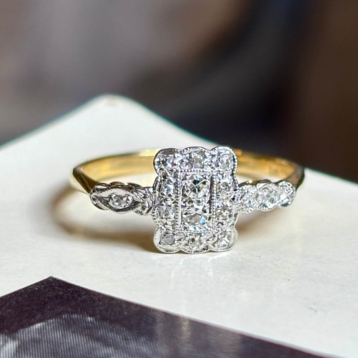 Antique, Edwardian diamond panel cluster engagement ring placed on vintage book with blurred background