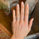 Antique, Edwardian diamond panel cluster engagement ring worn on hand with blurred background 