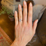 A hand wearing an Edwardian daisy diamond cluster ring with an 18ct yellow gold band with a blurred background