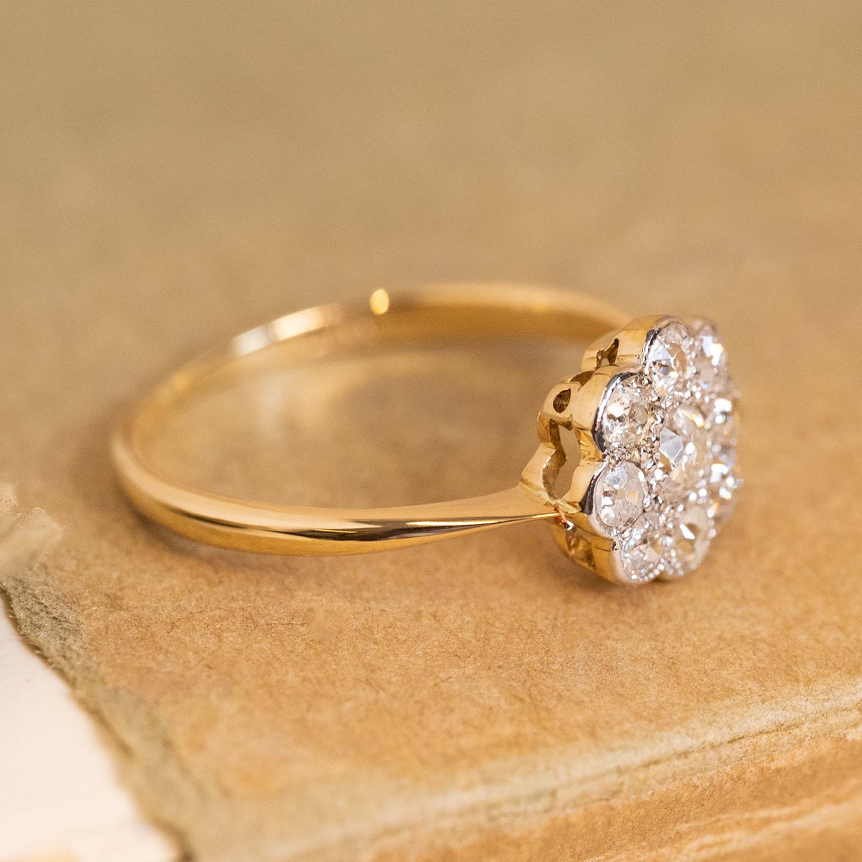 A gold antique Edwardian ring with a rub-over setting featuring 9 old-cut diamonds in a daisy cluster arrangement. 