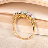 A yellow gold ring with opal stones set with diamonds in yellow gold, showing engraved scrolls on the setting on a book background. 