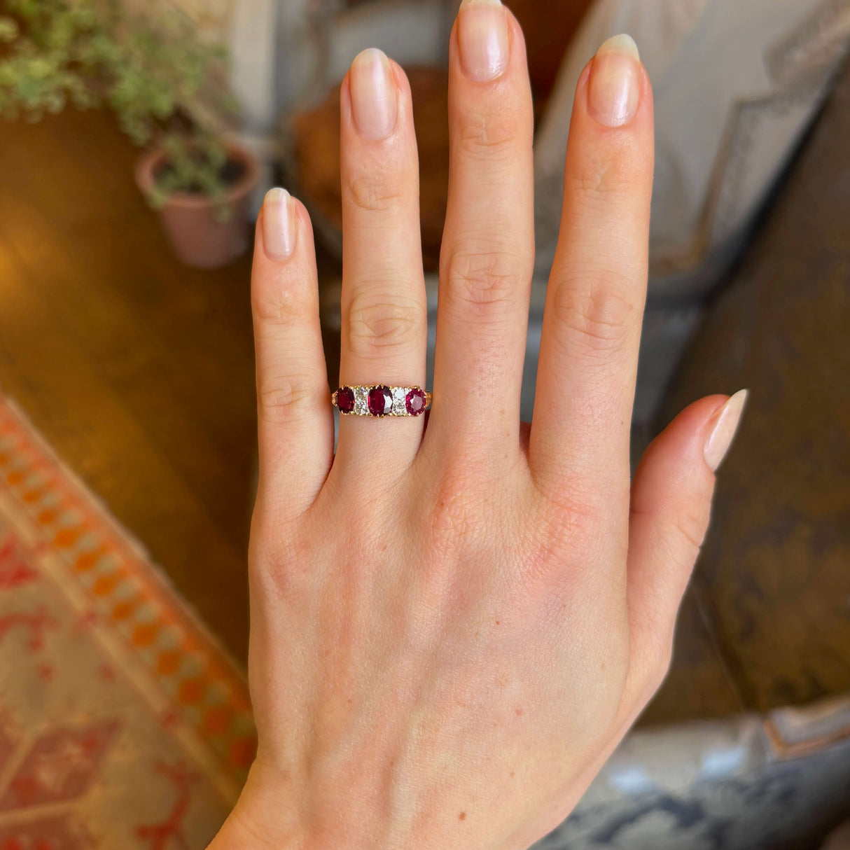 Antique, Victorian ruby and diamond three-stone ring worn on ring finger of left hand with blurred background

