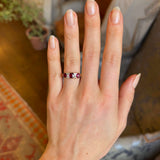 Antique, Victorian ruby and diamond three-stone ring worn on ring finger of left hand with blurred background
