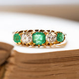Antique yellow gold ring with five gemstones including emeralds and diamonds on old book pages.