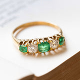 Gold five-stone ring with three luminous green emeralds and two old-mine cut diamonds on a old book page.