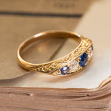 A Victorian five stone ring with blue sapphires and diamonds set in yellow gold with intricate engraved scroll details.